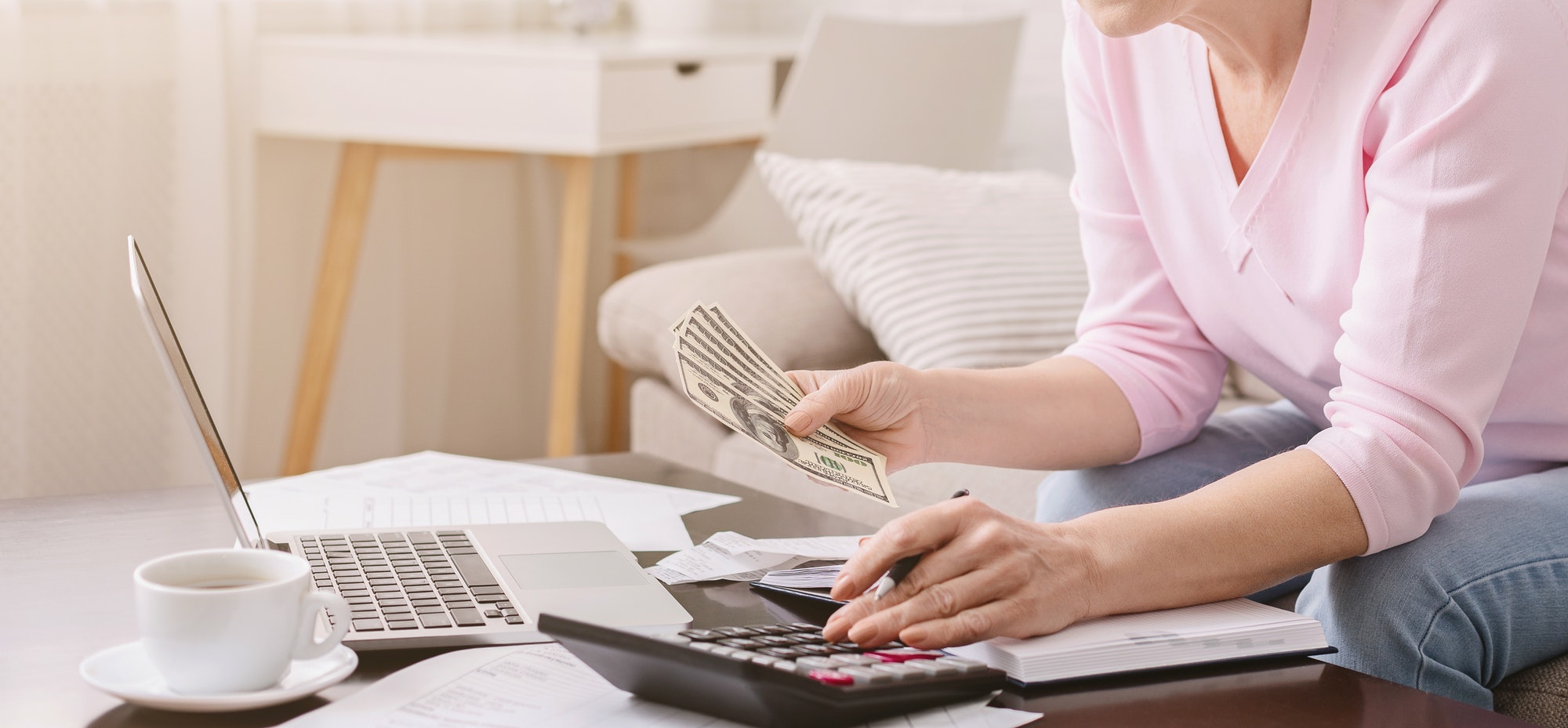 Senior woman with calculator counting dollar money at home